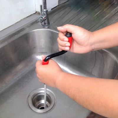 A budget drain engineer unblocking a sink using drain snake.
